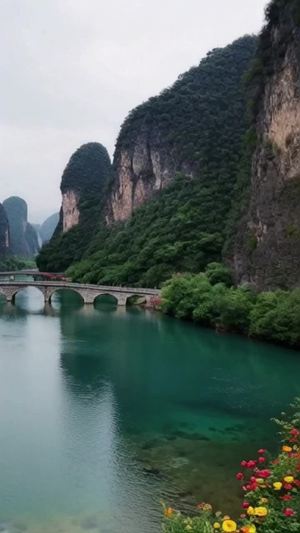 宁静的桂林山水，漓江的水清澈见底，两岸的山峰形态各异，山与山连接着石桥，山脚周边长满了花儿，天空阴沉，